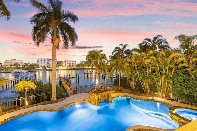 pool at dusk featuring boat lift, a dock, a water view, fence, and a pool with connected hot tub