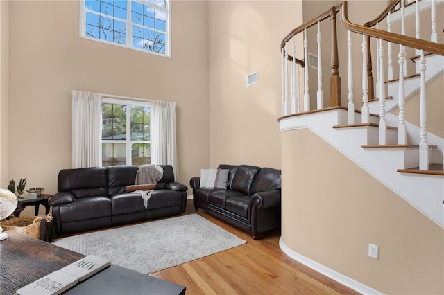 living area featuring a towering ceiling, stairs, visible vents, and wood finished floors