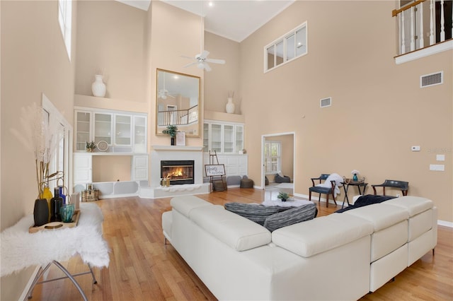 living area featuring light wood-type flooring, a glass covered fireplace, visible vents, and a healthy amount of sunlight