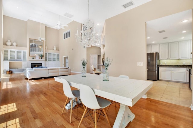 dining room with a warm lit fireplace, ceiling fan with notable chandelier, visible vents, and light wood-style floors