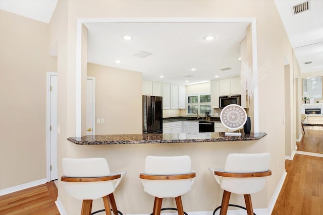 kitchen featuring black appliances, light wood finished floors, a peninsula, and visible vents