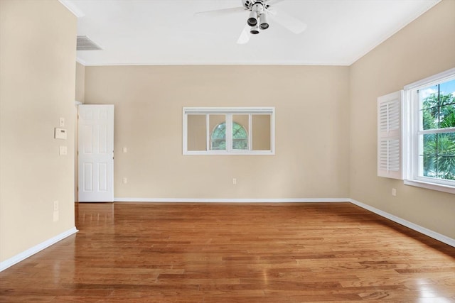 empty room featuring baseboards, visible vents, a ceiling fan, wood finished floors, and crown molding