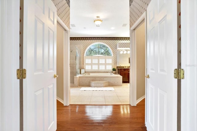 full bath with wood finished floors, baseboards, a tile shower, a bath, and wallpapered walls