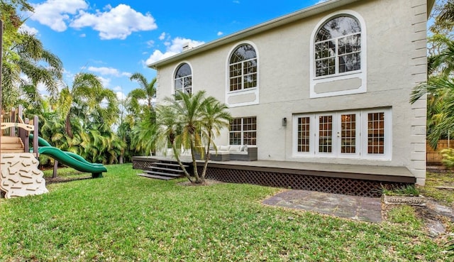 back of property featuring a playground, a lawn, and stucco siding