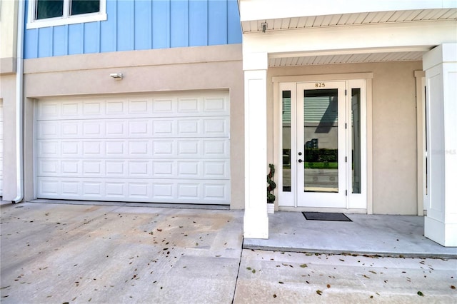 view of exterior entry with an attached garage, concrete driveway, board and batten siding, and stucco siding