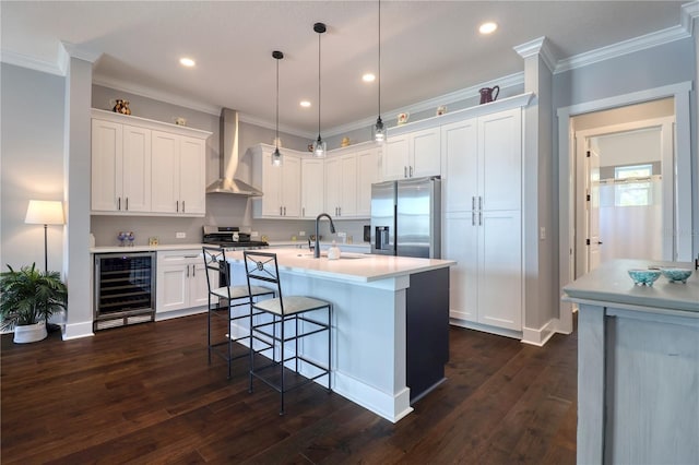 kitchen with beverage cooler, a sink, light countertops, wall chimney range hood, and appliances with stainless steel finishes