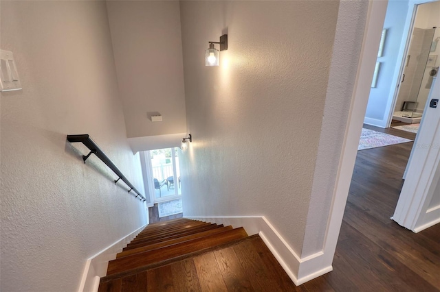 stairs featuring baseboards, wood finished floors, and a textured wall