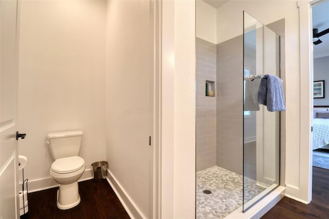 full bathroom with toilet, baseboards, wood finished floors, and tiled shower