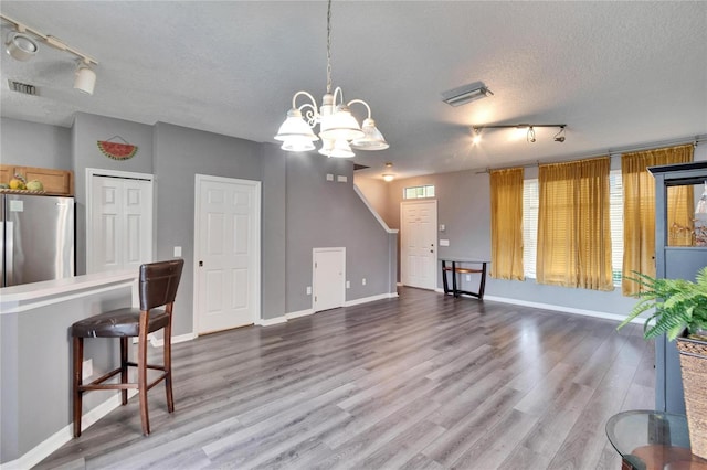 kitchen with a textured ceiling, wood finished floors, visible vents, a kitchen breakfast bar, and freestanding refrigerator