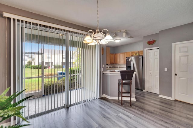 kitchen featuring stainless steel fridge, tasteful backsplash, wood finished floors, a peninsula, and a chandelier