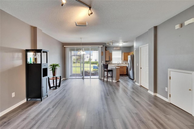 unfurnished living room featuring visible vents, a sink, a textured ceiling, and wood finished floors