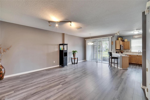 unfurnished living room with a notable chandelier, a sink, visible vents, baseboards, and light wood-style floors