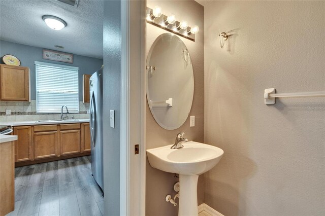 bathroom featuring a textured ceiling, wood finished floors, a sink, and decorative backsplash