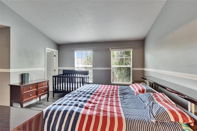 bedroom with a textured ceiling, vaulted ceiling, and wood finished floors