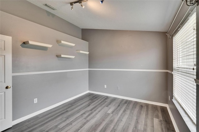 empty room with rail lighting, wood finished floors, visible vents, and baseboards