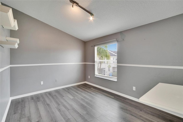 spare room featuring lofted ceiling, a textured ceiling, track lighting, wood finished floors, and baseboards