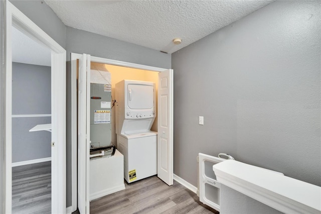 clothes washing area featuring stacked washer and clothes dryer, light wood-style flooring, a textured ceiling, laundry area, and baseboards