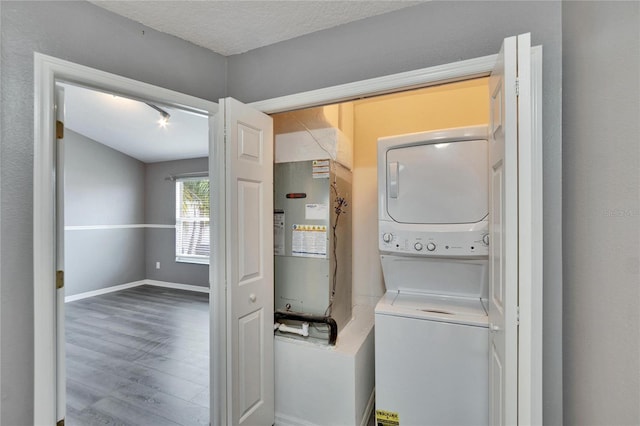 washroom with a textured ceiling, laundry area, wood finished floors, baseboards, and stacked washing maching and dryer