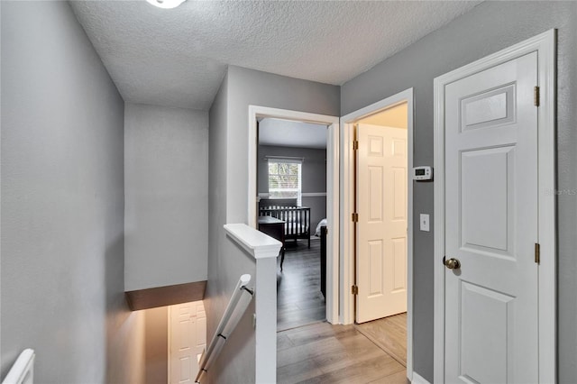 hall featuring a textured ceiling, light wood-style flooring, and an upstairs landing