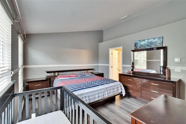 bedroom with a textured ceiling, vaulted ceiling, and wood finished floors