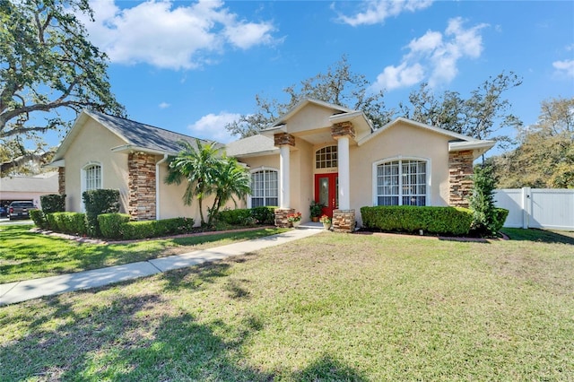 view of front of house with stucco siding, a front yard, a gate, fence, and stone siding