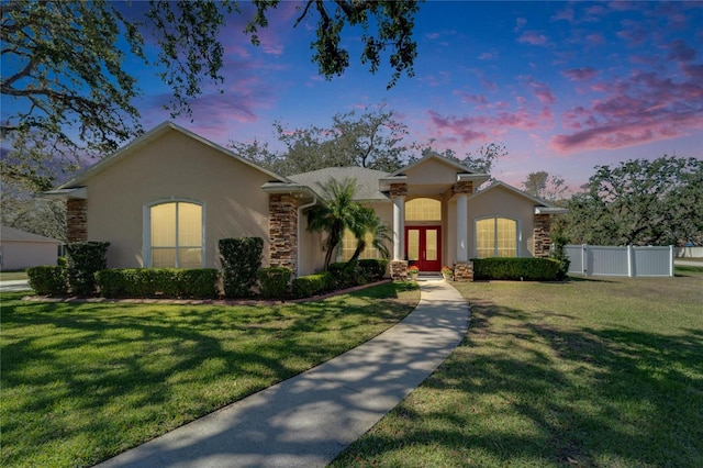 view of front facade featuring a lawn, fence, french doors, and stucco siding