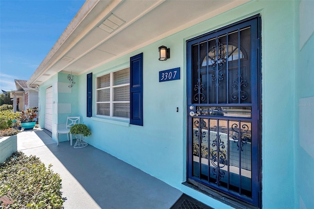 entrance to property with a garage and stucco siding