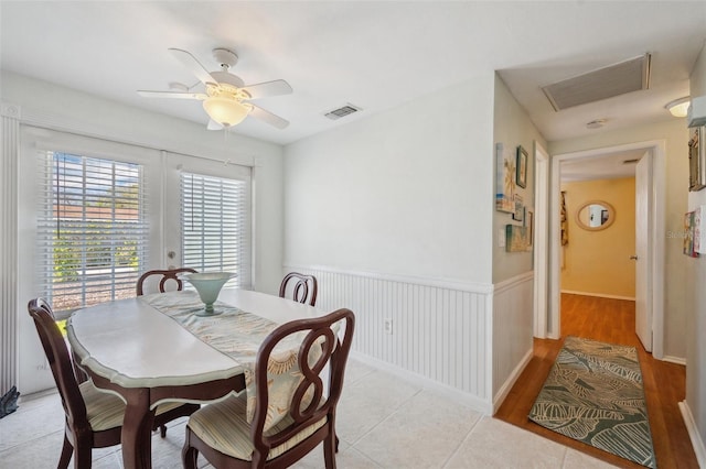 dining space with light tile patterned floors, a wainscoted wall, visible vents, a ceiling fan, and french doors