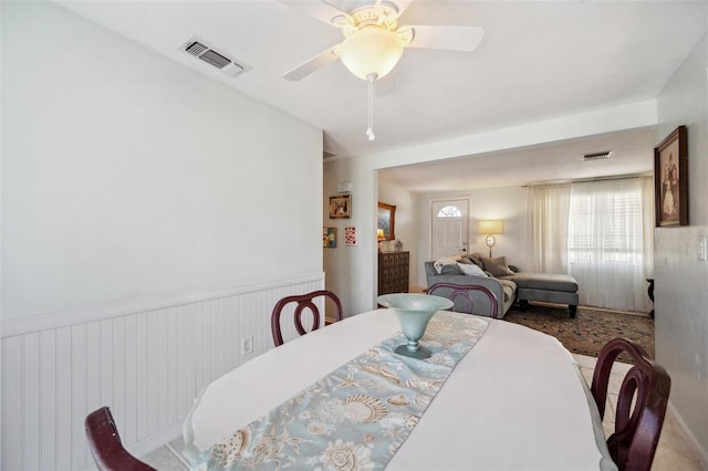 dining area with a wainscoted wall, ceiling fan, and visible vents