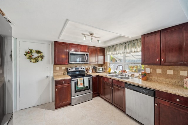 kitchen with light countertops, appliances with stainless steel finishes, reddish brown cabinets, tasteful backsplash, and a raised ceiling