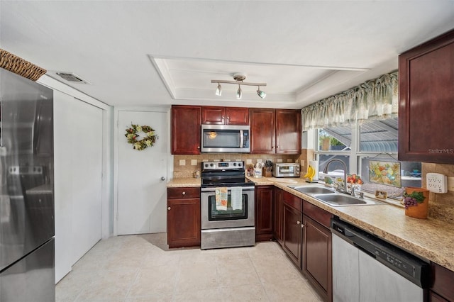 kitchen with a sink, light countertops, appliances with stainless steel finishes, reddish brown cabinets, and tasteful backsplash