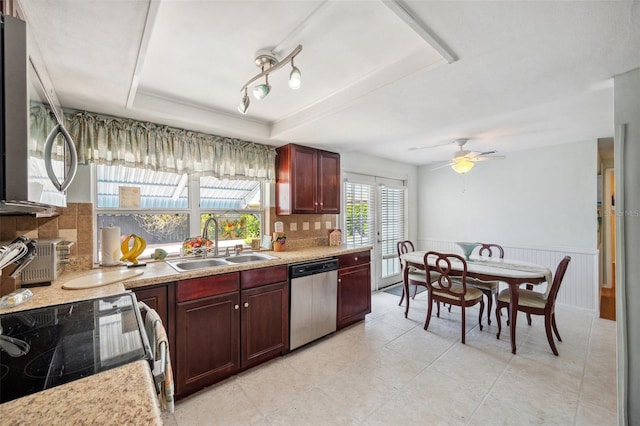 kitchen featuring a sink, appliances with stainless steel finishes, wainscoting, backsplash, and a tray ceiling