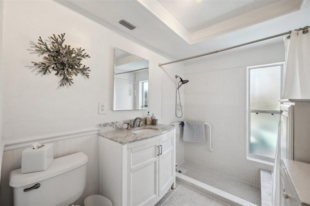 bathroom featuring toilet, a wainscoted wall, vanity, visible vents, and tiled shower