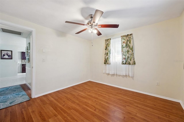 spare room featuring a ceiling fan, wood finished floors, visible vents, and baseboards