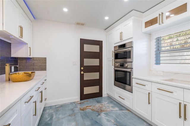 kitchen with visible vents, white cabinetry, stainless steel double oven, light countertops, and decorative backsplash