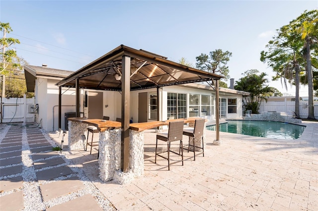 view of patio featuring outdoor dry bar, fence, a gazebo, a fenced in pool, and central AC unit