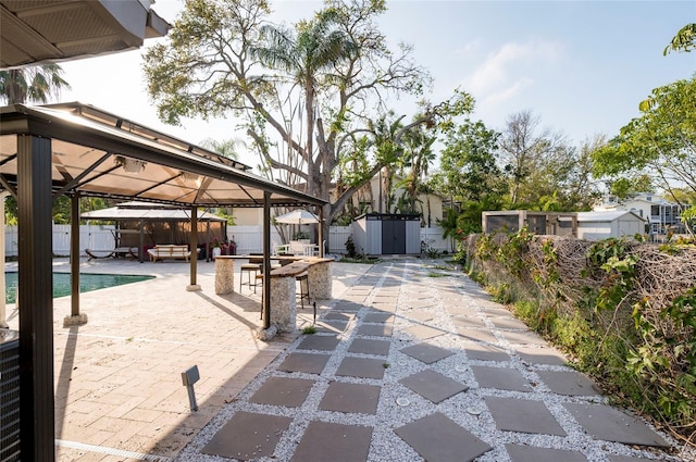 view of patio featuring a gazebo, a fenced backyard, a storage shed, and an outbuilding