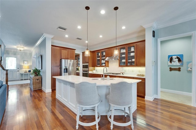 5616 Seagrass Pl, Apollo Beach, FL 33572 - kitchen featuring light countertops, appliances with stainless steel finishes, brown cabinets, an island with sink, and glass insert cabinets