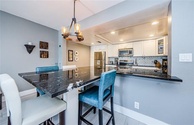 kitchen with glass insert cabinets, white cabinetry, appliances with stainless steel finishes, a peninsula, and decorative backsplash