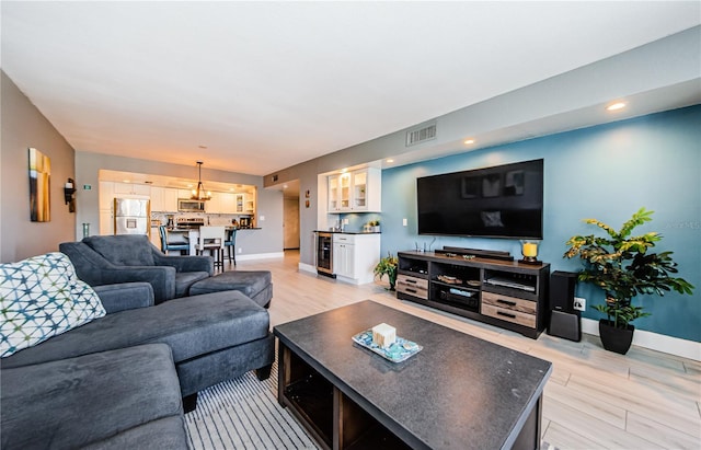 living room with beverage cooler, visible vents, light wood finished floors, and baseboards