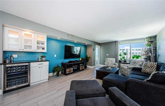 living area with wine cooler, light wood finished floors, a bar, and baseboards