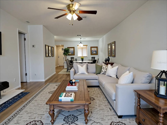 living area featuring baseboards, a ceiling fan, visible vents, and wood finished floors