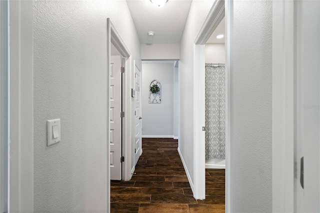 hallway with a textured wall, baseboards, and wood finish floors