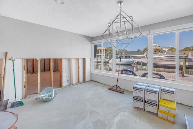 dining area featuring a water view, a textured ceiling, concrete floors, and a notable chandelier