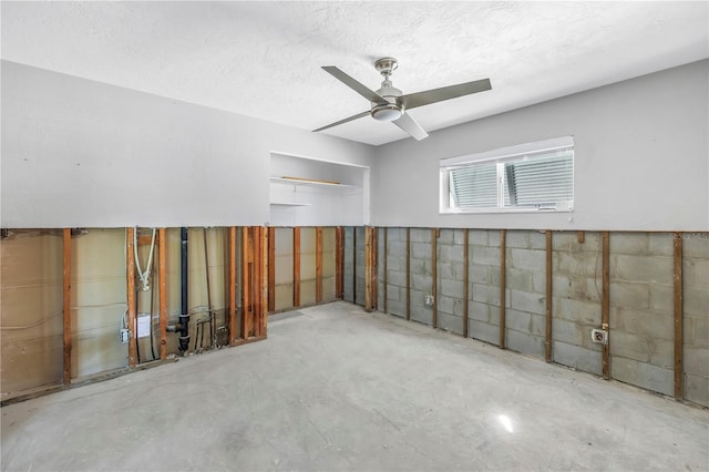 spare room with a textured ceiling, concrete floors, a ceiling fan, and concrete block wall