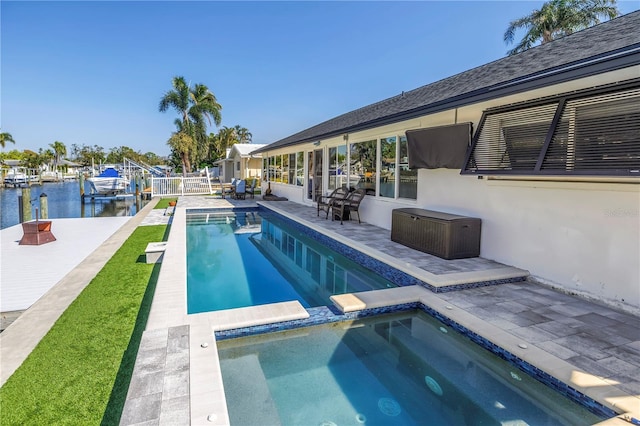 pool featuring a patio area, a water view, fence, and an in ground hot tub