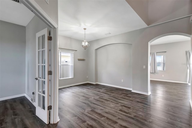 empty room with dark wood-type flooring, arched walkways, baseboards, and an inviting chandelier