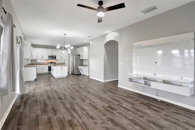 unfurnished living room featuring baseboards, visible vents, arched walkways, dark wood-type flooring, and ceiling fan with notable chandelier