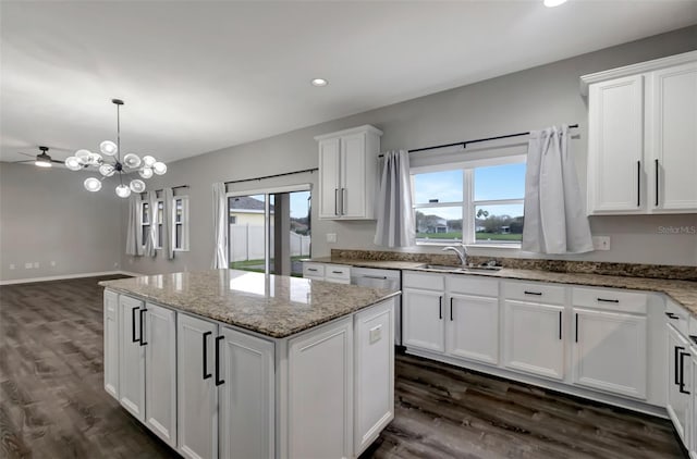 kitchen featuring dark wood finished floors, light stone counters, a center island, white cabinetry, and a sink