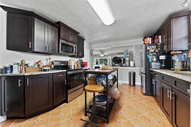 kitchen featuring light stone counters, appliances with stainless steel finishes, a textured ceiling, and a ceiling fan